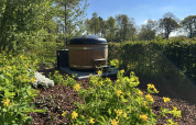 Trætønde-spabad i en frodig have ved tiny house Anthropod i ferieparken 't Rheezerwold, Holland.