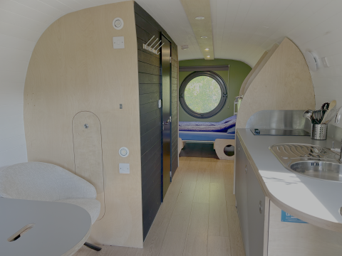 Intérieur de la tiny house Anthropod au parc de vacances 't Rheezerwold aux Pays-Bas, avec fenêtre ronde et cuisine.