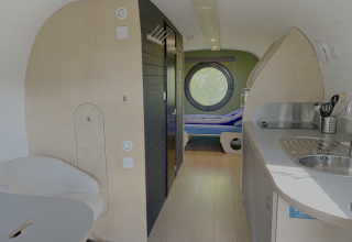 Interieur van het tiny house Anthropod in vakantiepark 't Rheezerwold in Nederland, met ronde raam en keuken.