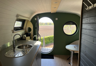 Interieur van Anthropod tiny house op vakantiepark 't Rheezerwold, met keuken en uitzicht op een veld in Nederland.