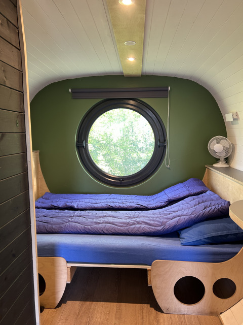 Vista interior de una tiny house llamada Anthropod con ventana redonda y cama en los Países Bajos.