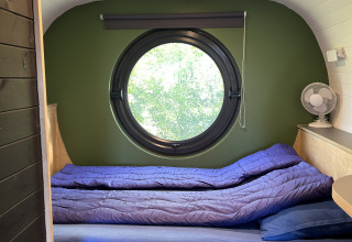 Vista interior de una tiny house llamada Anthropod con ventana redonda y cama en los Países Bajos.