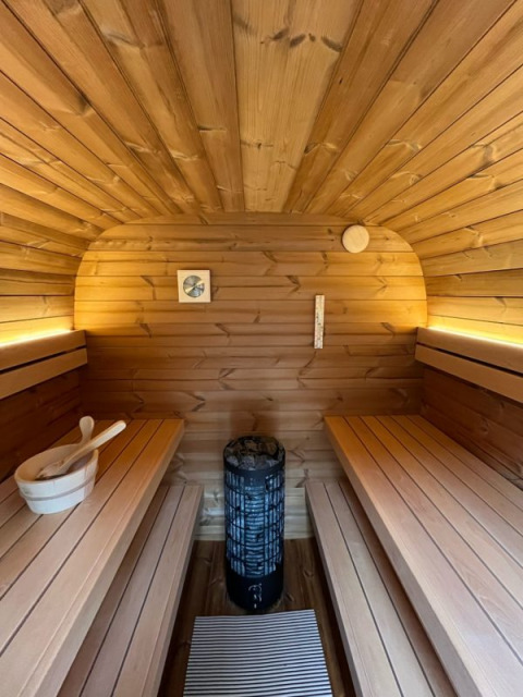 Houten saunaruimte op een woonboot, met tegenoverliggende banken, kachel, houten emmer en warme verlichting.