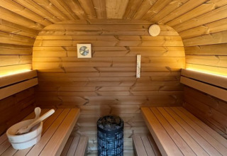 Innenraum einer Sauna auf einem Hausboot mit Holzbänken, Saunaofen, Schüssel und warmem Licht.