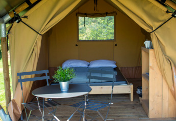 Safari telt Duo Lodge på Campsite de Boomgaard i Belgien, med seng, bord, stole og trædæk udenfor.