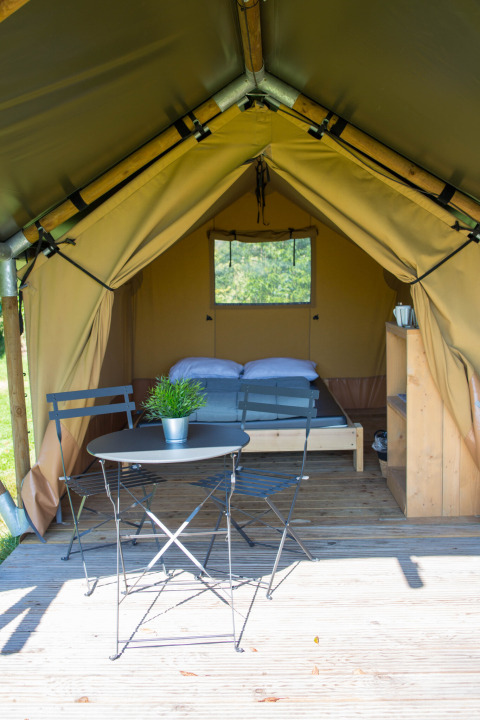 Safari-Zelt Duo Lodge auf dem Campingplatz de Boomgaard in Belgien mit Bett, Tisch, Stühlen und Holzterrasse.