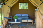 Tenda safari Duo Lodge al campeggio de Boomgaard in Belgio con letto, tavolo, sedie e terrazza in legno.