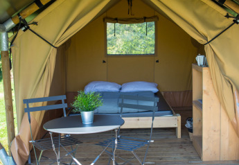 Safari tent Duo Lodge at Campsite de Boomgaard in Belgium with bed, table, chairs, and wooden deck outside.