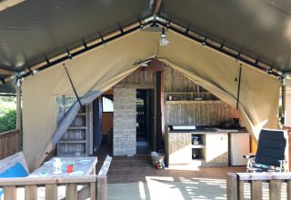 Interior de una tienda safari en el camping de Kerleyou, Francia, con mesa de comedor, cocina y zona de descanso.
