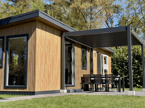 Tiny house moderne Forest Lodge, bardage bois, terrasse couverte et coin repas extérieur en pleine nature.