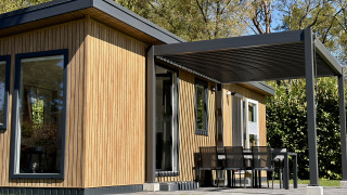Casa pequeña y moderna llamada Forest Lodge, con techo cubierto, fachada de madera y comedor exterior.