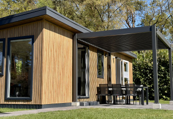 Casa pequeña y moderna llamada Forest Lodge, con techo cubierto, fachada de madera y comedor exterior.