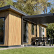 Tiny house moderna chiamata Forest Lodge con rivestimento in legno e patio coperto immersa nella natura.