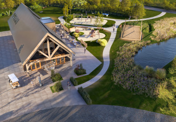 Vue aérienne d’un lodge au bord d’un lac avec chemins, aire de jeux et espaces verts entourés de nature.