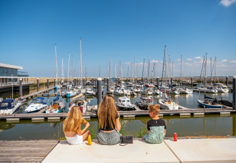 Tre børn sidder og nyder udsigten over havnen med lystbåde ved Duinlodge 6, EuroParcs Cadzand-Bad.
