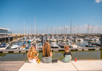 Trois enfants assis, admirant le port et les voiliers à Duinlodge 6, EuroParcs Cadzand-Bad, Pays-Bas.