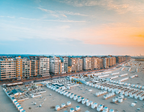 Vista panoramica su un lungomare moderno con palazzi e cabine bianche sulla spiaggia al tramonto.