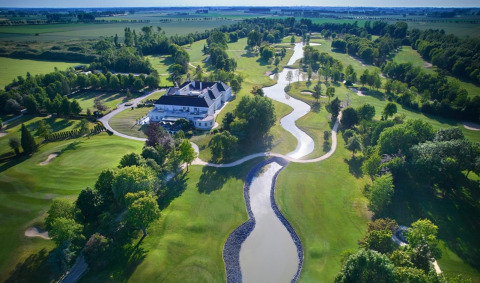 Vista aerea di un grande lodge immerso in un campo da golf verdeggiante con torrenti sinuosi in campagna.
