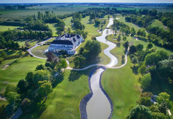 Vue aérienne d’un vaste lodge entouré d’un parcours de golf verdoyant et de cours d’eau ondulants en campagne.