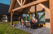 Familie isst gemeinsam draußen bei Duinvilla 8 im EuroParcs Cadzand-Bad, Niederlande, bei schönem Wetter.