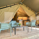 Tenda safari con terrazza in legno, cucina moderna e quattro sedie blu per un soggiorno confortevole.