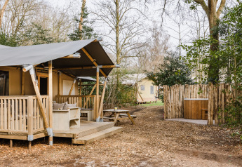 Tienda safari 'De Stille Heide' en Gooise Heide, Países Bajos, rodeada de árboles y jacuzzi exterior.