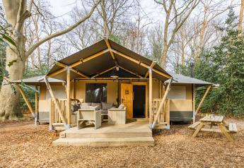 Tienda safari ‘De Stille Heide’ en Gooise Heide, Países Bajos, con terraza de madera y asientos afuera.