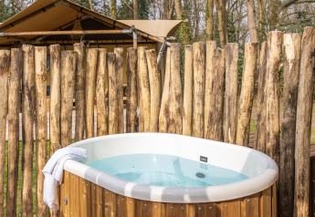 Baignoire extérieure devant une tente safari à De Bos Escape, Gooise Heide, Pays-Bas, entourée d'une palissade en bois.