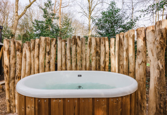 Jacuzzi exterior junto a la tienda safari «De Stille Heide» en Gooise Heide, Países Bajos, rodeado de troncos.
