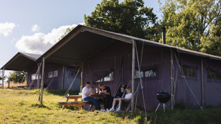 Gezin aan tafel bij safaritent op BoerenBed Het Wesselink in Salland, Nederland, geniet van het buitenleven.