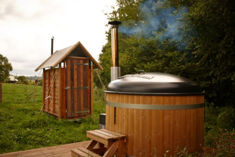 Safarizelt mit privater Dusche neben dem Zelt und Hot Tub in natürlicher, grüner Umgebung.