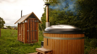 Safari tent cottage with private hot shower next to the tent and hot tub in a lush, green setting.