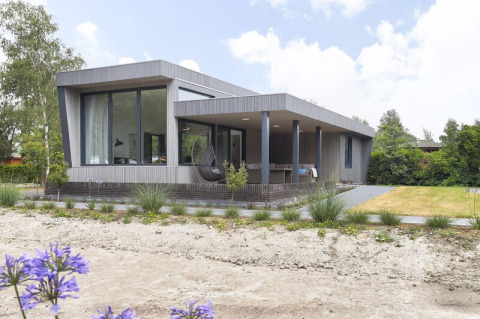 Moderne Boslodge Plus med veranda og have ved feriecenter 't Schuttenbelt, omgivet af grønne træer.
