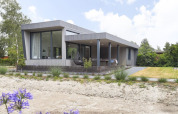 Moderne Boslodge Plus med veranda og have ved feriecenter 't Schuttenbelt, omgivet af grønne træer.