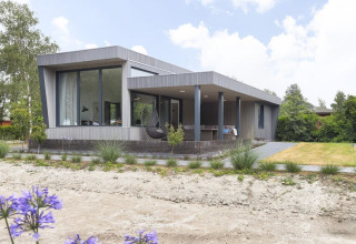 Modern Boslodge Plus with veranda and garden at Holiday center 't Schuttenbelt, surrounded by trees.