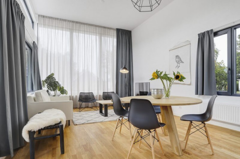 Heldere, moderne leefruimte in Boslodge Plus met grote ramen, eettafel, zonnebloemen en sofa.