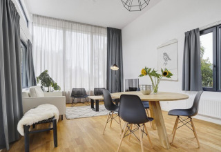 Lichte, moderne woonkamer in Boslodge Plus met grote ramen, eettafel, zonnebloemen en bank.