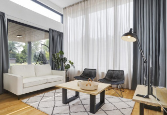 Sala moderna en Boslodge Plus met Hottub con ventanales altos, sofá blanco y sillas negras en Países Bajos.