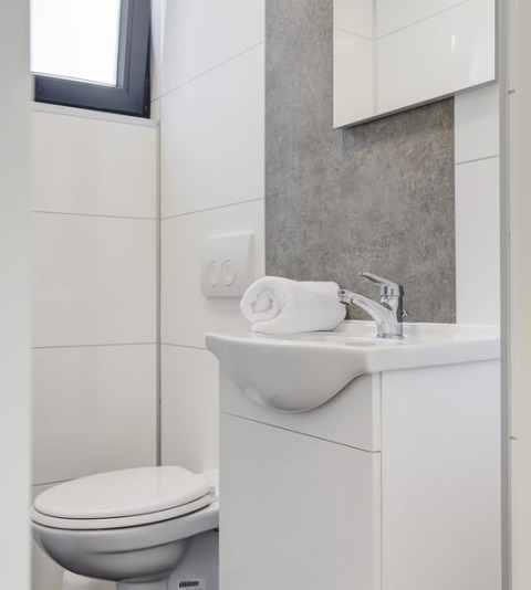 Moderne, compacte badkamer met een wit toilet, wastafel en een netjes opgerolde handdoek op de wastafel.