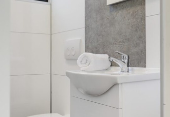 Baño moderno y compacto con inodoro blanco, lavabo y una toalla enrollada cuidadosamente sobre el lavabo.