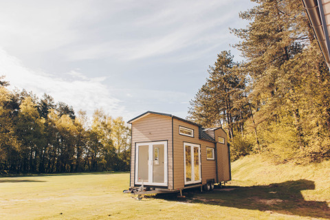 En moderne tiny house ved navn Koya Tiny Loft står i naturen omgivet af grønne træer og åben himmel.