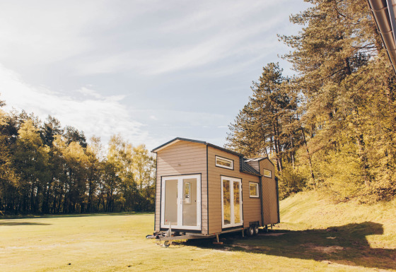 En moderne tiny house ved navn Koya Tiny Loft står i naturen omgivet af grønne træer og åben himmel.