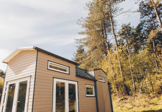 Lille træhus kaldet Koya Tiny Loft beliggende ved Wilsumer Berge, omgivet af grønne træer i Tyskland.
