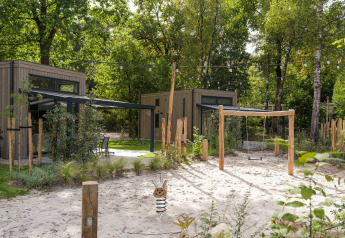 Moderne Tiny Houses im Veluwe Park de Bosgraaf, Niederlande, mit Spielplatz und umgeben von Wald.
