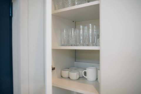 Een kast in het tiny house Rosendael bij Veluwe park de Bosgraaf, Nederland, met glazen en mokken.