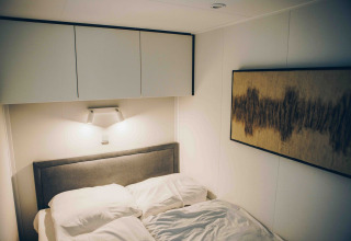 Slaapkamer van tiny house met opbergkasten, kunst en verlichting in Veluwe park de Bosgraaf, Nederland.