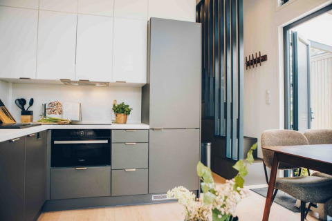 Moderne tiny house keuken met grijze en witte kasten, oven, eettafel en veel natuurlijk licht.