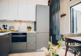 Moderne tiny house keuken met grijze en witte kasten, oven, eettafel en veel natuurlijk licht.