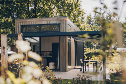 Moderne tiny house Rosendael met overdekt terras en tuin, omringd door bomen en veel groen.