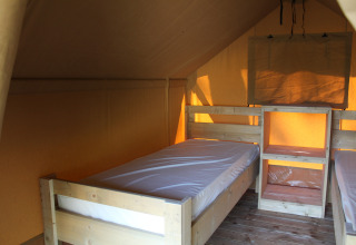 Intérieur d'une tente safari avec lits en bois au Camping La Colline en Belgique, éclairée par le soleil.